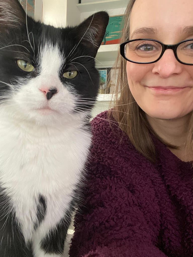 Rachel Jackson Marketing Tech Specialist a head shot of Rachel who is smiling and next to her is Beans the cat who is staring at the camera. Beans is a black and white tuxedo cat.