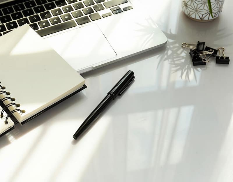 Black and white image of a desk set up with a laptop pen and note pad
